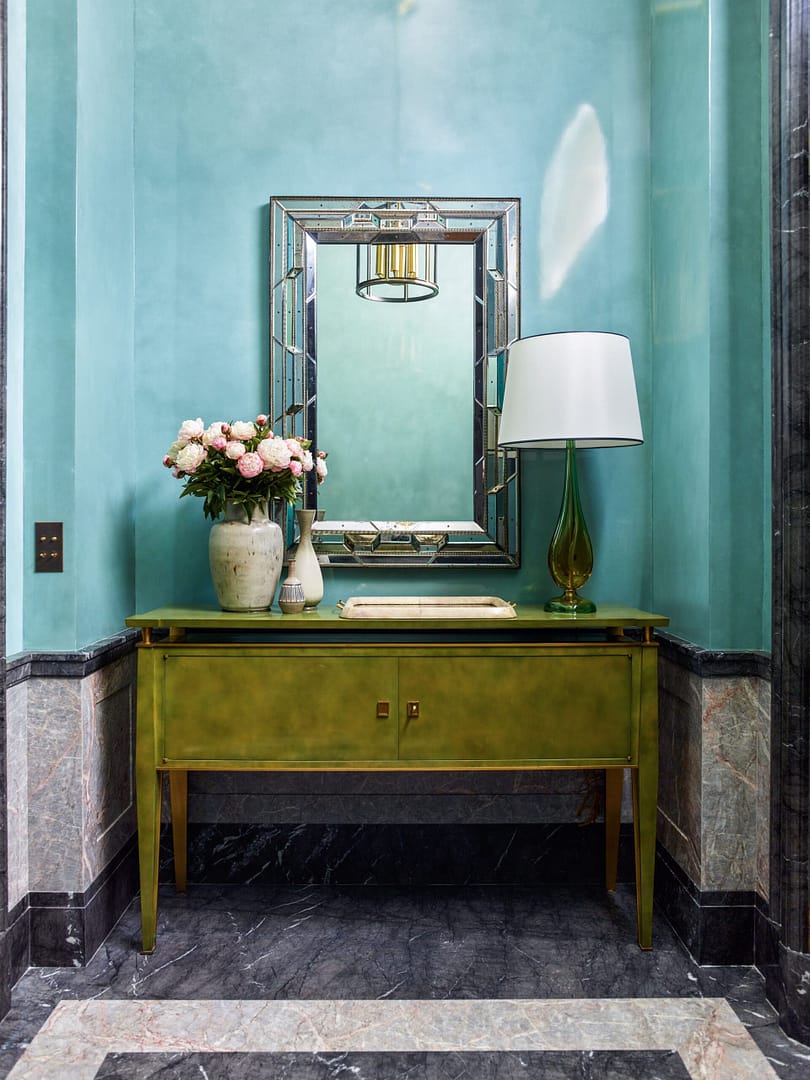 A green dresser in a hallway with a mirror.