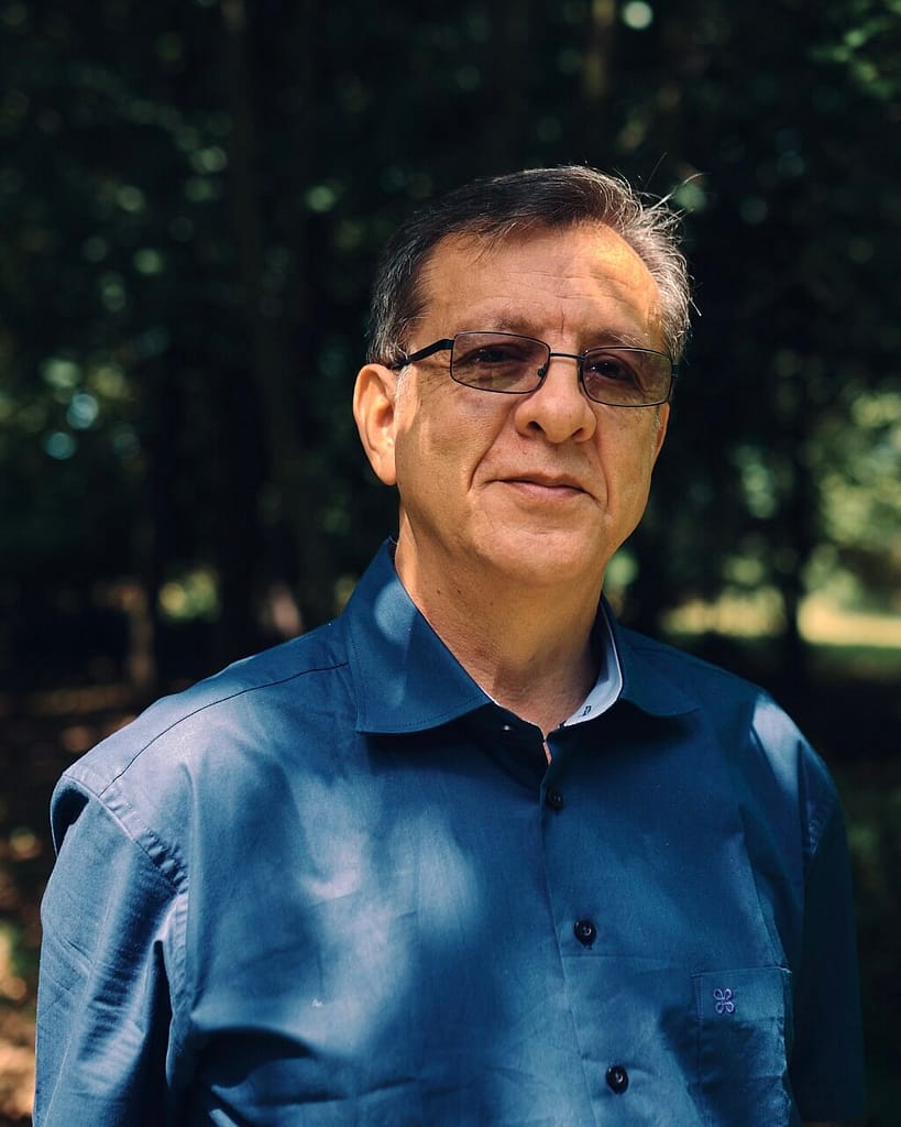 Dr. Luis Eduardo Luna in a blue shirt standing in a wooded area.