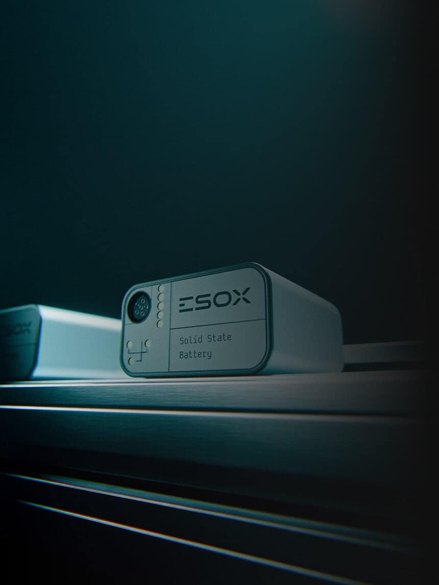 A close-up of a rectangular device labeled "ESOX Solid State Battery" resting on a metallic surface, with another similar device partially visible in the background. The scene is dimly lit with a blue tint.