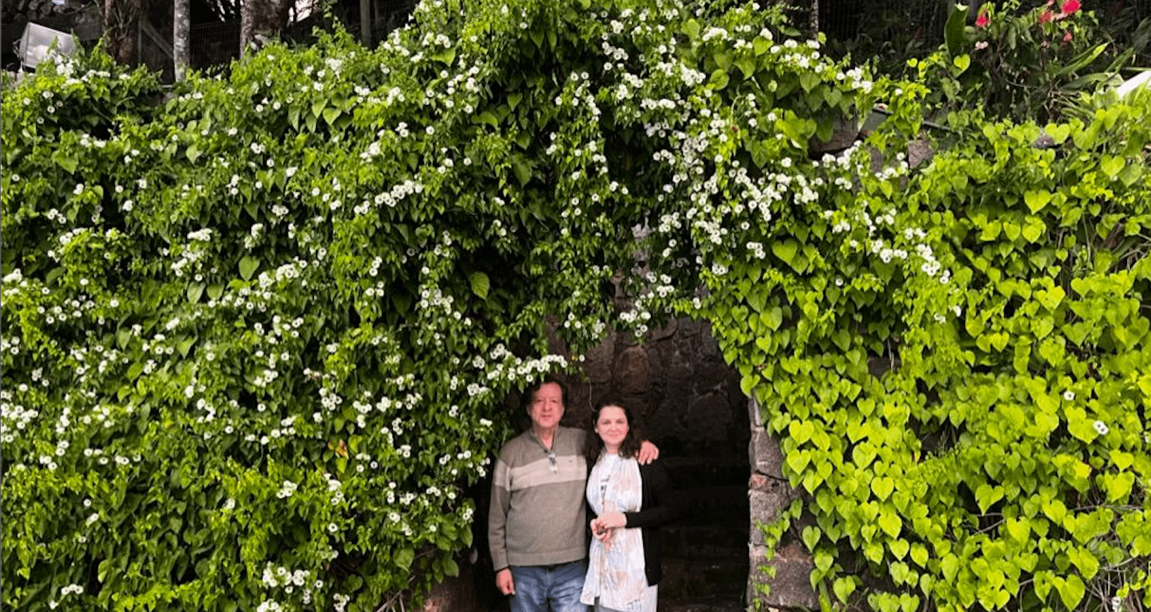 A man and woman standing in front of a stone archway.